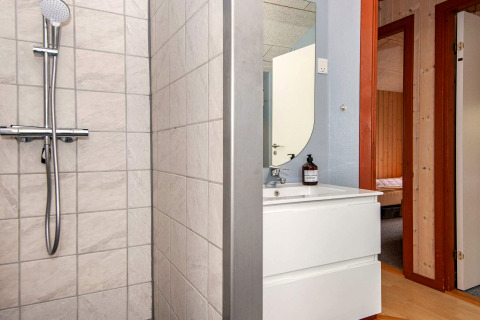 Salle de bain avec douche, lavabo et miroir dans une maison de vacances à Haderslev, Danemark. Porte visible.