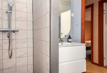 Salle de bain avec douche, lavabo et miroir dans une maison de vacances à Haderslev, Danemark. Porte visible.