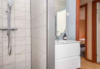 Salle de bain avec douche, lavabo et miroir dans une maison de vacances à Haderslev, Danemark. Porte visible.