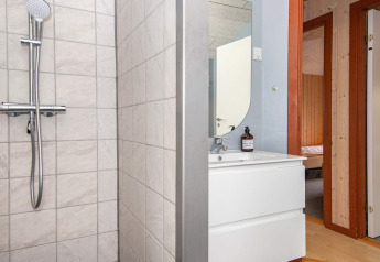 Baño con ducha, lavabo y espejo en casa de vacaciones en Haderslev, Dinamarca. Se ve la puerta del dormitorio.
