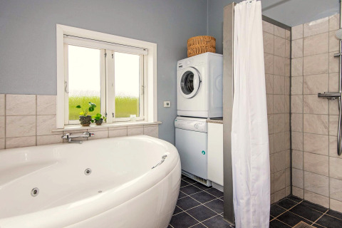 Badezimmer mit Eckbadewanne, Dusche, Waschmaschine, Trockner und Fenster in einem Haus in Haderslev.