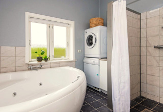 Bagno con vasca ad angolo, doccia, lavatrice, asciugatrice e finestra in una casa vacanze a Haderslev.