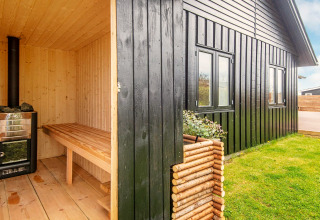 Sauna esterna in legno accanto a casa vacanze nera con prato a Haderslev, Danimarca.