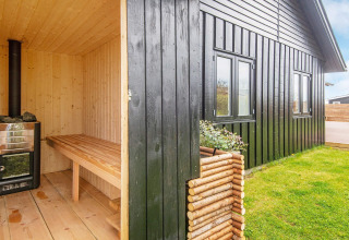 Sauna extérieur en bois à côté d'un gîte noir avec pelouse à Haderslev, au Danemark.