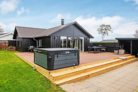 Lodge de vacances noir à Haderslev avec terrasse en bois, spa extérieur, coin repas et pelouse.