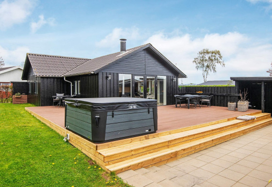 Lodge de vacances noir à Haderslev avec terrasse en bois, spa extérieur, coin repas et pelouse.