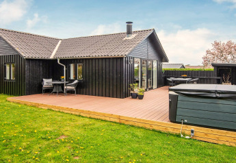Maison de vacances noire avec grande terrasse et jacuzzi, située dans un cadre verdoyant à Haderslev, Danemark.