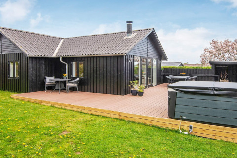 Maison de vacances noire avec grande terrasse et jacuzzi, située dans un cadre verdoyant à Haderslev, Danemark.