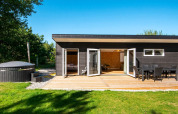 Sort feriehus med udendørs terrasse, spisebord, grøn have og spabad, beliggende i Glesborg, Danmark.