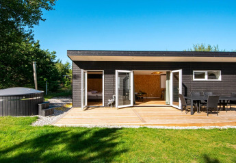 Maison de vacances noire avec terrasse, jacuzzi, mobilier d’extérieur et pelouse à Glesborg, Danemark.