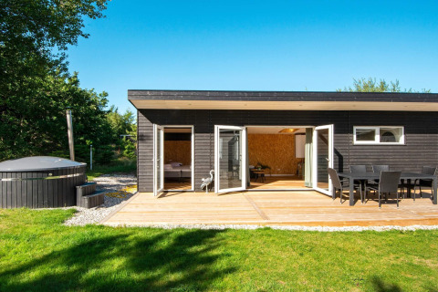 Sort feriehus med udendørs terrasse, spisebord, grøn have og spabad, beliggende i Glesborg, Danmark.