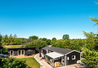 Maison de vacances à Glesborg, Danemark, entourée de verdure, terrasse, véranda et ciel bleu éclatant.