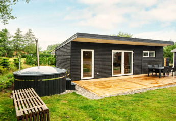 Maison de vacances noire moderne à Glesborg, Danemark, avec terrasse, coin repas et bain à remous extérieur.