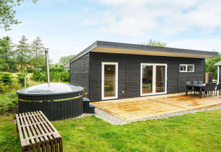 Moderne sort træferiebolig i Glesborg, Danmark, med terrasse, spisebord og udendørs vildmarksbad.