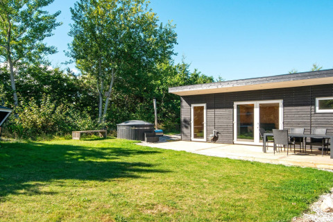 Udendørsbillede af en moderne feriebolig i Glesborg, Danmark, med terrasse, havemøbler og grøn have.