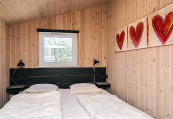Dormitorio con cama doble, paredes de madera y arte de corazones en una casa de vacaciones en Glesborg, Dinamarca.