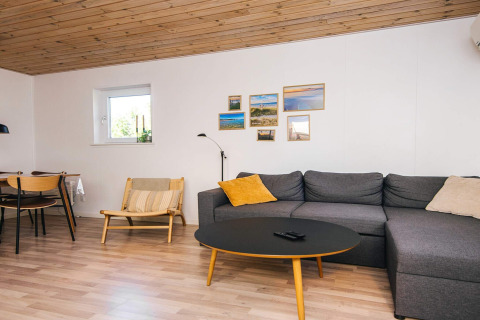 Stue med træloft, gråt hjørnesofa, sort sofabord og billedvæg i fempersoners feriehus i Glesborg, Danmark.