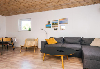 Wohnzimmer mit Holzdecke, grauem Ecksofa, schwarzem Couchtisch und Wandbildern in Glesborg, Dänemark.