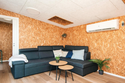 Moderne stue i feriehus i Glesborg, Danmark, med hjørnesofa, runde borde, planter og aircondition.
