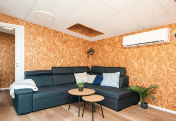 Moderne stue i feriehus i Glesborg, Danmark, med hjørnesofa, runde borde, planter og aircondition.