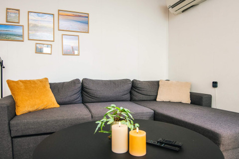 Hyggelig stue i feriehus med grå sofa, farvede puder, billeder på væggen og dekorationslys på bordet.