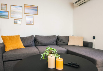 Hyggelig stue i feriehus med grå sofa, farvede puder, billeder på væggen og dekorationslys på bordet.