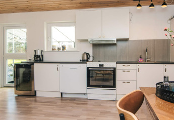 Moderne Küche mit weißen Schränken, Backofen und Essbereich im Ferienhaus in Glesborg, Dänemark.