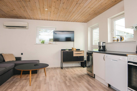 Stue og køkkenområde i feriebolig i Glesborg, Danmark, med sofagruppe, TV og moderne køkken.