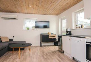 Stue og køkkenområde i feriebolig i Glesborg, Danmark, med sofagruppe, TV og moderne køkken.