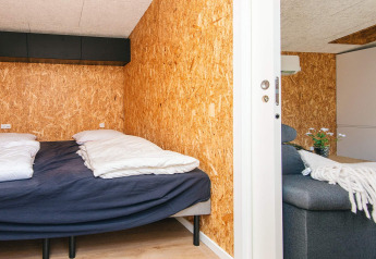 Slaapkamer en woonkamer in een vakantiehuis in Glesborg, Denemarken, met spaanplaten muren.