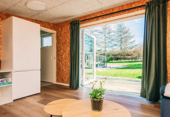 Salon d'une maison de vacances à Glesborg, Danemark, avec portes ouvertes sur jardin et terrasse ensoleillée.