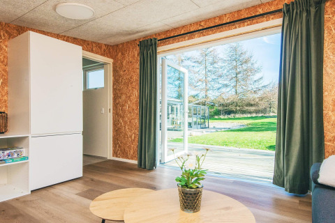 Stue i feriebolig i Glesborg, Danmark, med åbne døre til terrasse, grøn have og store vinduer.