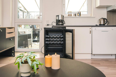 Moderne køkken med åben vinkøler, kaffemaskine, stearinlys og plante i feriebolig i Glesborg, Danmark.