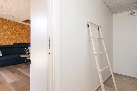 Indretning af feriehus i Glesborg, Danmark, med stige mod væg og moderne opholdsområde med sofa.