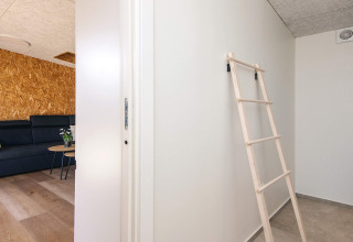 Indretning af feriehus i Glesborg, Danmark, med stige mod væg og moderne opholdsområde med sofa.