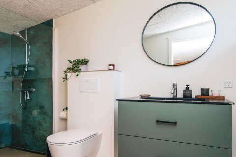 Moderne badeværelse i feriehus i Glesborg, Danmark, med grøn brusekabine, toilet og rund spejl.
