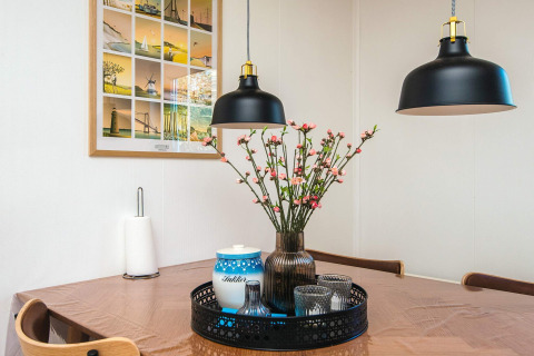 Spisebord i dansk feriehus med blomster, lamper, vægbillede, papirholder og bakke i Glesborg.