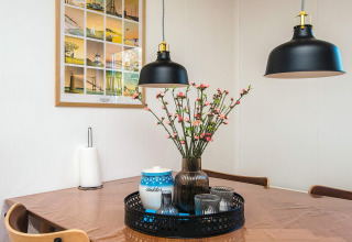 Spisebord i dansk feriehus med blomster, lamper, vægbillede, papirholder og bakke i Glesborg.
