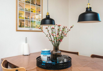 Eettafel in vakantiehuis in Glesborg, Denemarken met bloemen, lampen en een ingelijst kunstwerk.