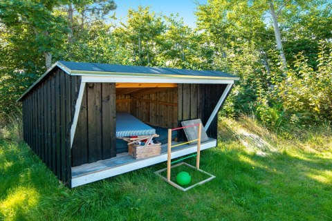 Et lille sort træskur med madras og kasse i grøn have ved ferieboligen 5 person holiday home i Glesborg, Danmark.
