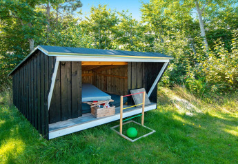 Kleine zwarte houten schuilhut met matras en kist op gras bij 5 person holiday home in Glesborg, Denemarken.