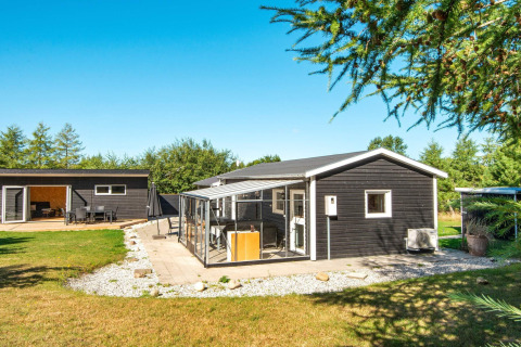Moderne sort feriebolig med udestue og have i Glesborg, Danmark, under en klar blå himmel.