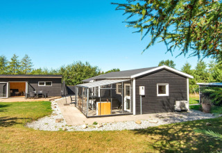 Moderne sort feriebolig med udestue og have i Glesborg, Danmark, under en klar blå himmel.