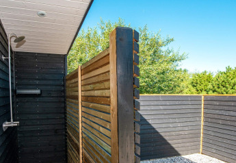 Douche extérieure à la maison de vacances avec panneaux en bois et vue sur les arbres verdoyants.