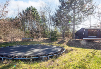 Trampoline en bank in de tuin bij vakantiehuis in Glesborg, Denemarken, met bomen en houten hut.