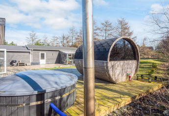 Buitenterras met hottub en barrelsauna bij 5-persoons vakantiehuis in Glesborg, Denemarken, omgeven door groen.