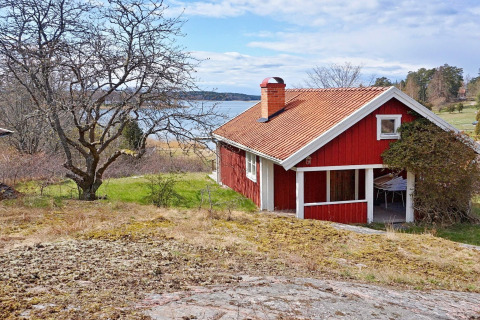 Casa vacanze rossa a Vaxholm, Svezia, situata vicino al lago e immersa nella natura verde.