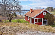 Rood Zweeds vakantiehuis in Vaxholm aan het meer, omgeven door natuur en bomen in een groene omgeving.