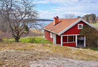 Casa vacanze rossa a Vaxholm, Svezia, situata vicino al lago e immersa nella natura verde.