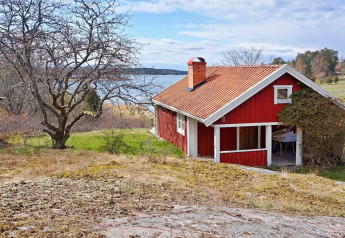 Rood Zweeds vakantiehuis in Vaxholm aan het meer, omgeven door natuur en bomen in een groene omgeving.
